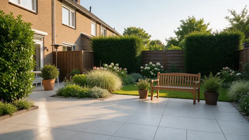 Verzorgde achtertuin met keramisch terras, houten schutting, borders en een tuinbank